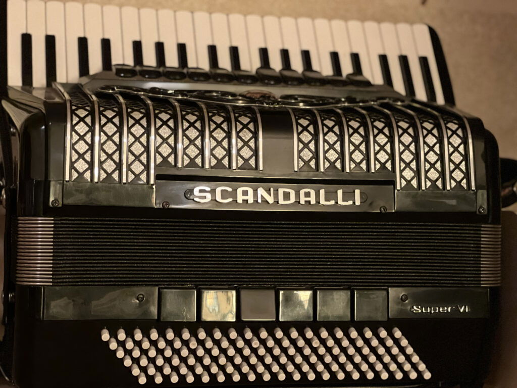 A close-up of a black Scandalli Super VI accordion, like those displayed in museums in Superior Wisconsin, showing its decorative grille, white and black piano keys, and multiple rows of white buttons.