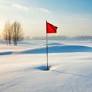 A red flag marks a golf hole on a snow-covered golf course, with bare trees and a soft sunrise or sunset in the background.