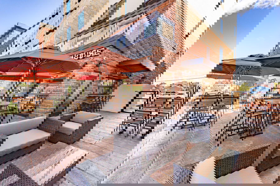 A distorted image of an outdoor restaurant patio with tables, chairs, and umbrellas evokes the atmosphere of a Lake Superior Ice Festival, digitally glitched with pixelated and warped sections throughout the scene.