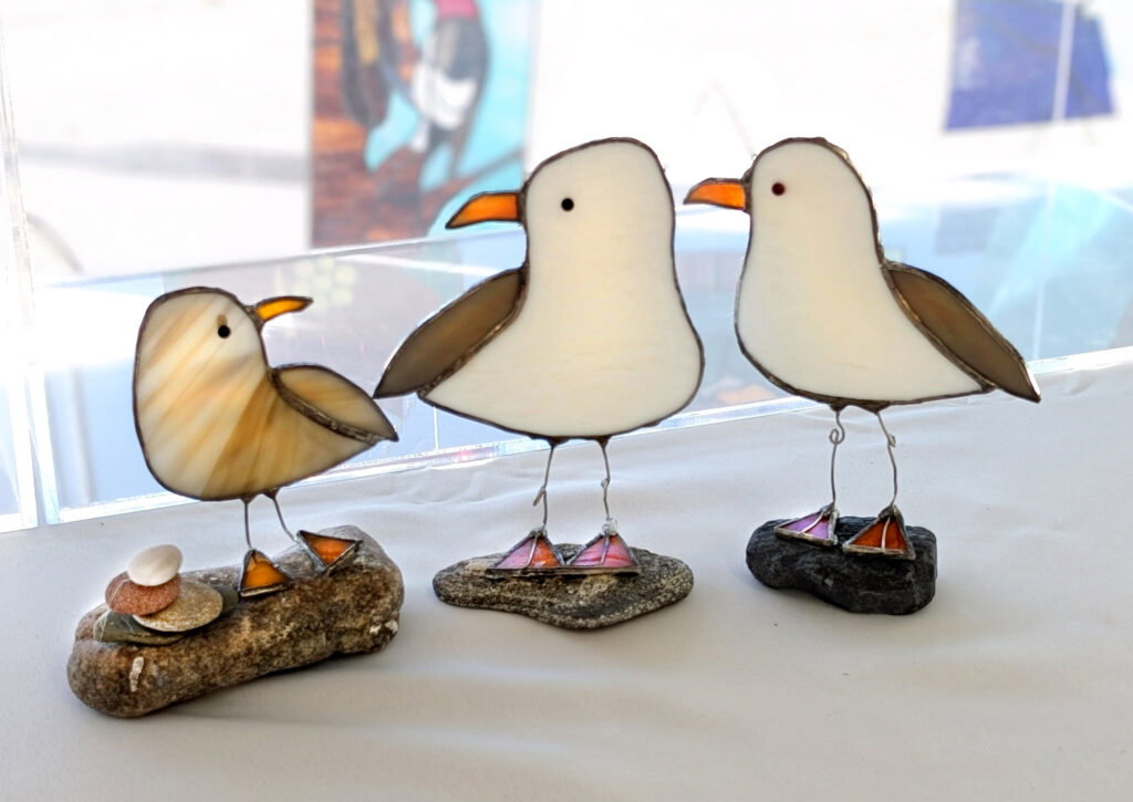 Two abstract, distorted birds with white and brown bodies stand on grey rocks against a blurry, multicolored background with light streaks and soft geometric shapes, evoking the vibrant spirit of the Lake Superior Ice Festival.