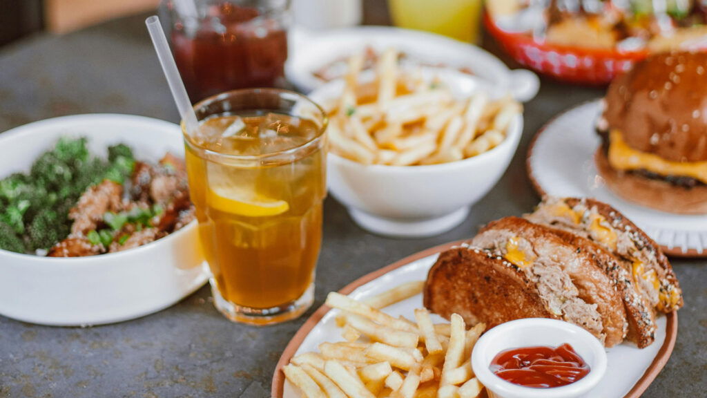 A table set with iced tea, a bowl of fries, a cheeseburger, a plate of sliced meatloaf sandwich with fries and ketchup, and a bowl of broccoli and chicken brings to mind the comfort food found at ethnic restaurants in Superior Wisconsin.