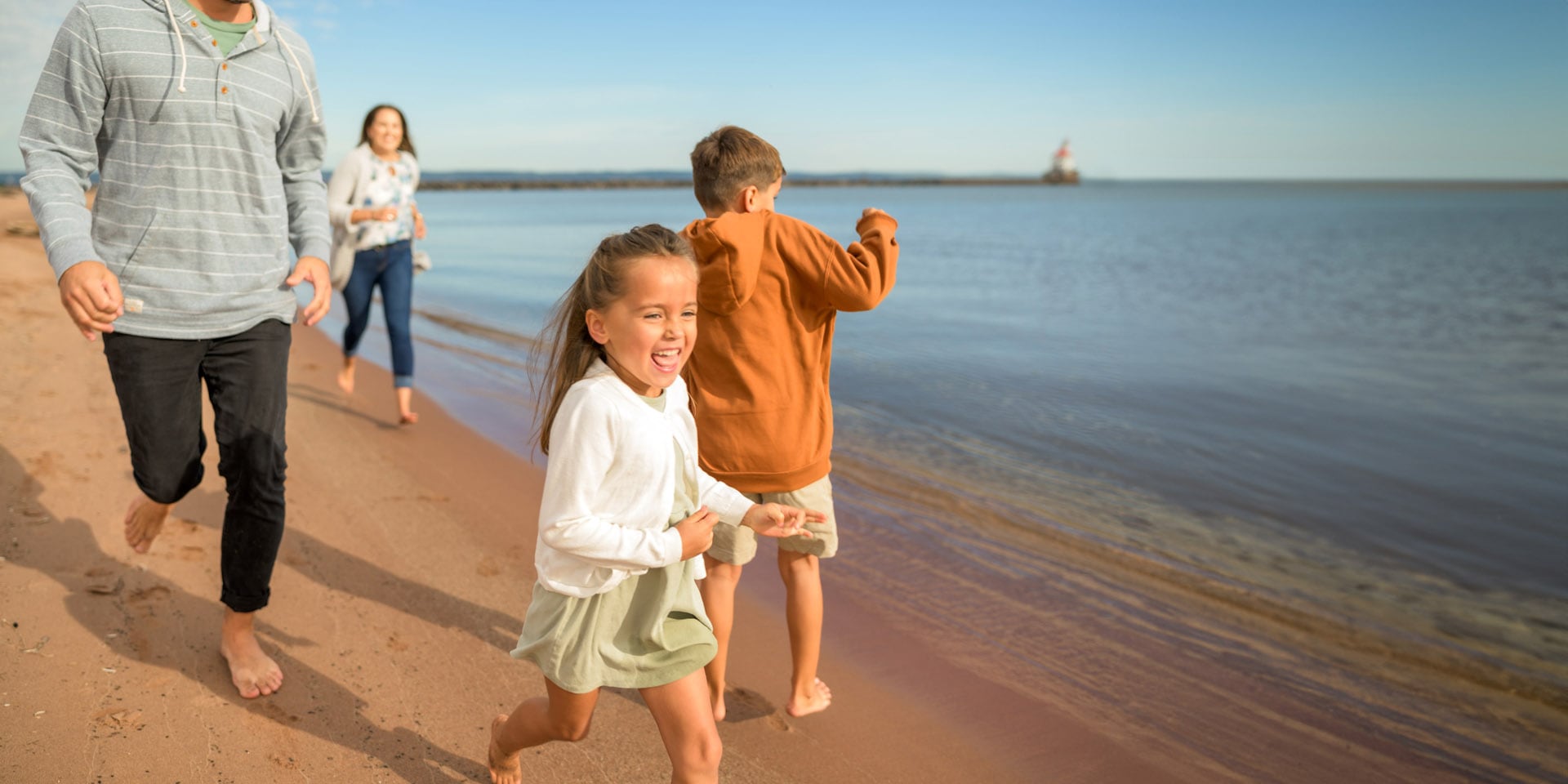 A family with two children runs barefoot along a sandy beach by the water on a sunny day, smiling and enjoying their time together—capturing the joy of weekend getaways in Wisconsin.