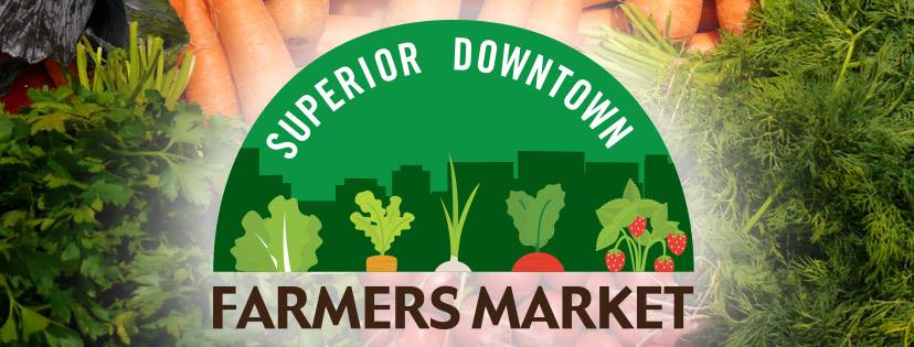 Logo for Superior Downtown Farmers Market featuring a green cityscape and illustrations of produce like lettuce, carrots, and strawberries, overlaid on a background of fresh vegetables such as carrots and herbs.
