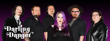 Six people stand in a row against a purple gradient background. The person in the center has long purple hair. All are dressed in dark clothing, and the words "Darling Danger" are displayed in stylized white text on the left.