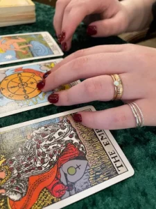 A hand with red nails and several rings spreads tarot cards, including The Empress, The Wheel of Fortune, and The Star, on a green surface—invoking a sense of mystery as vibrant as the spirit of holiday shopping in Superior Wisconsin.